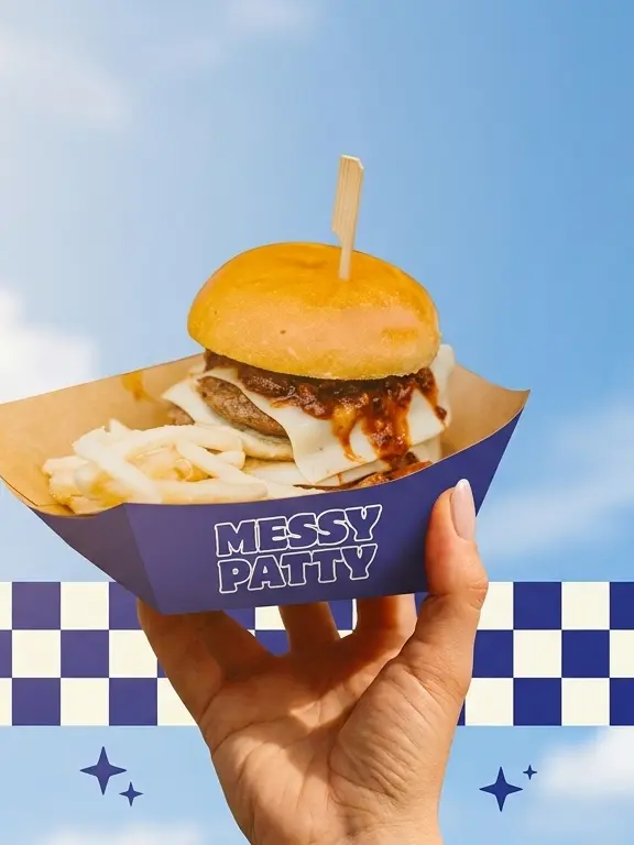 Chilli beef burger with melted cheese and fries in a Messy Patty paper boat, held up against the sky
