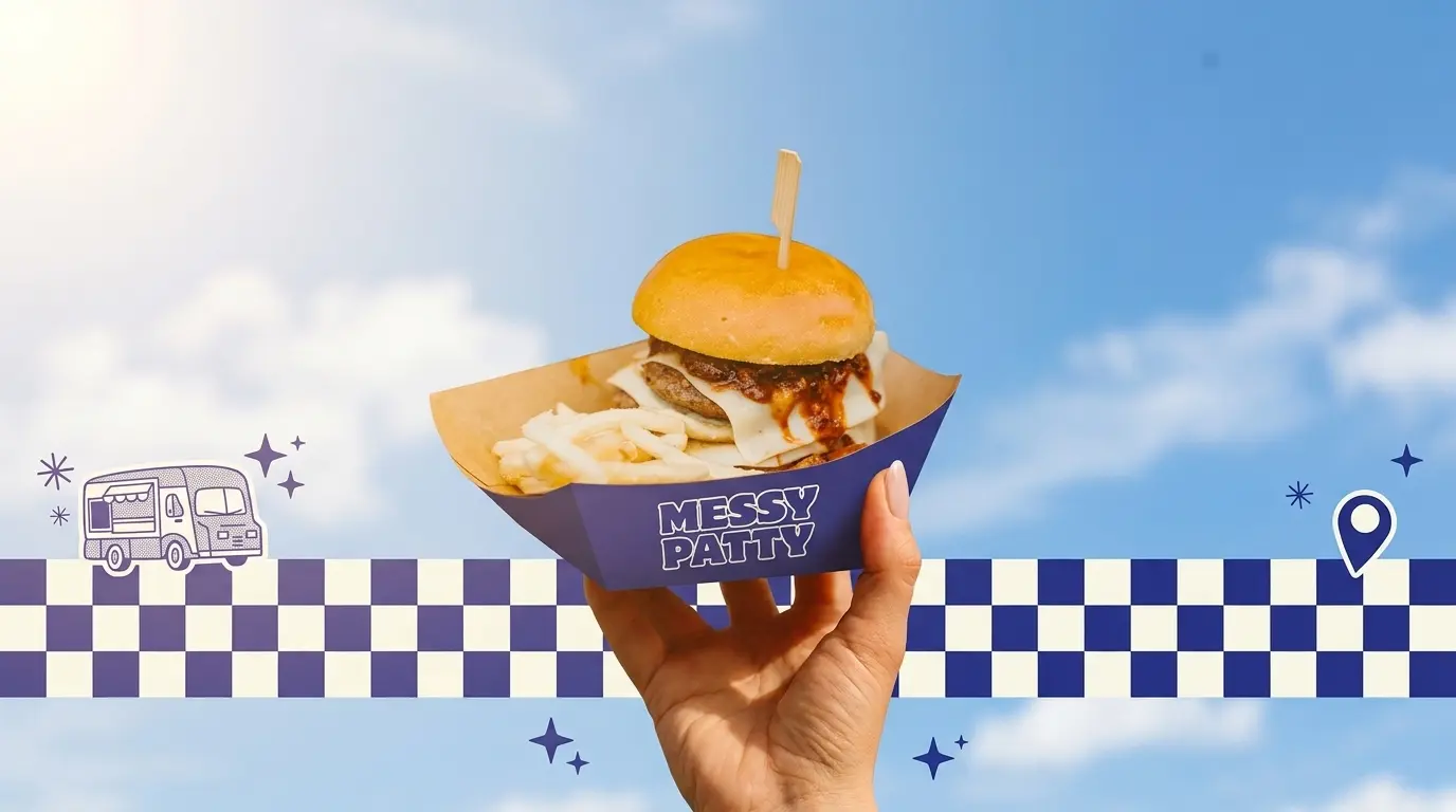 A hand holding up a burger and shoestring fries in a navy Messy Patty paper boat against a bright blue sky